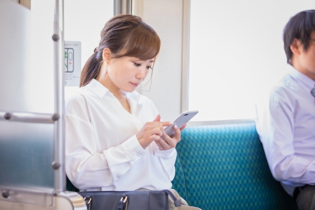 電車でスマートフォンを見ている女性の写真